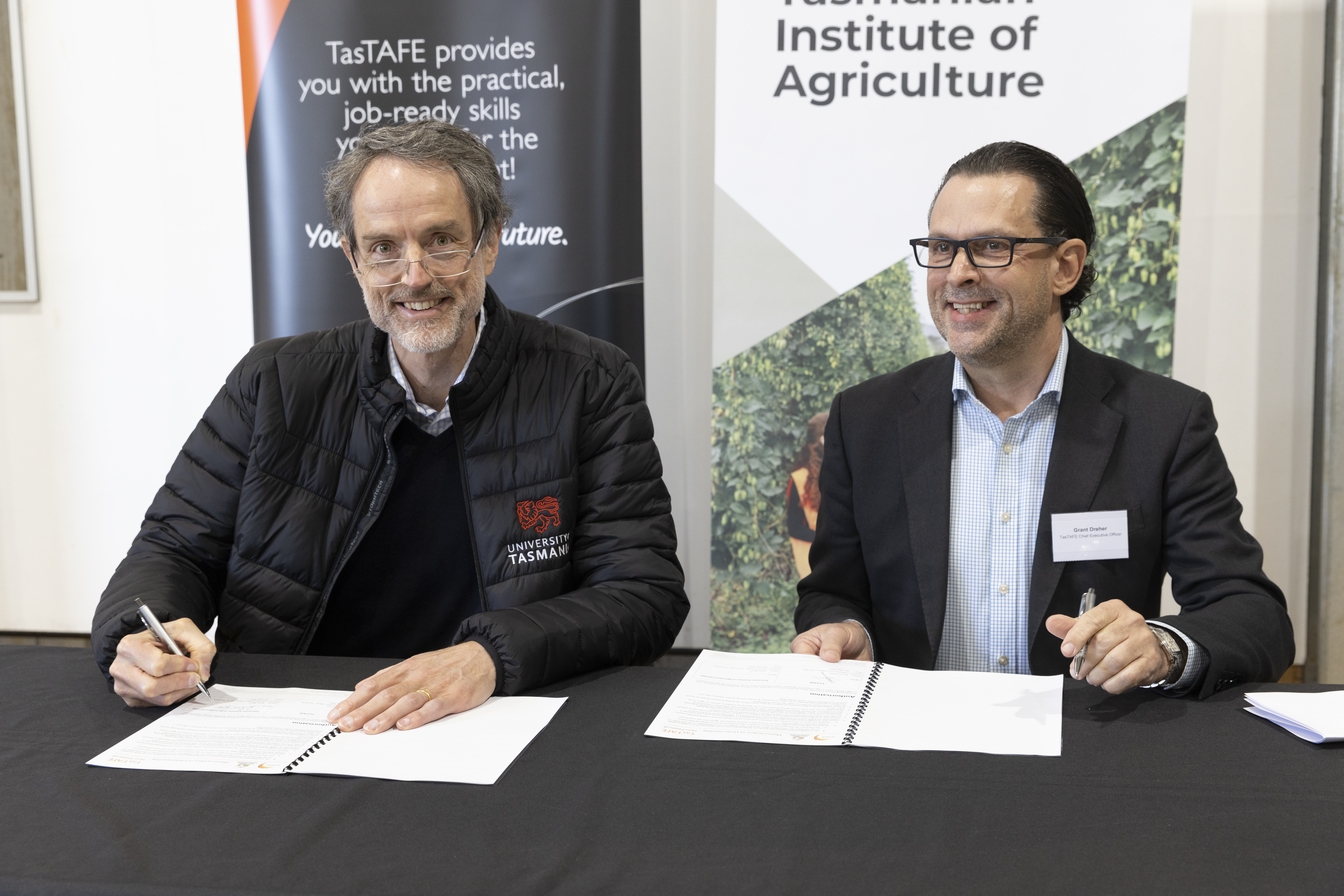 TasTAFE CEO Grant Dreher and University of Tasmania Vice Chancellor Rufus Black signing documents at a table