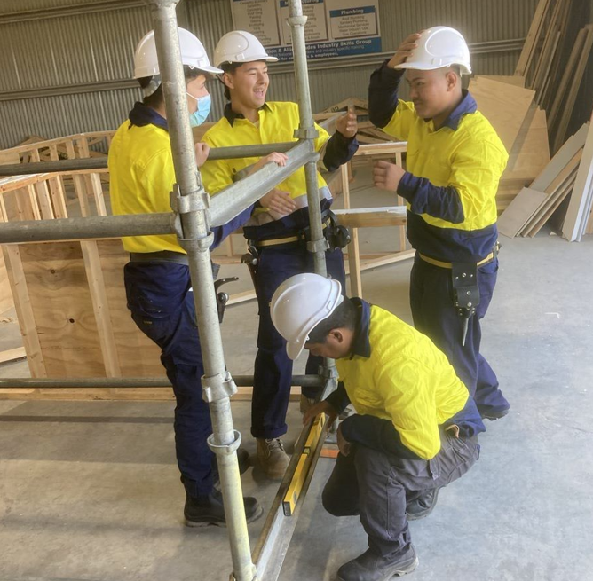 Four construction workers standing around some scaffolding