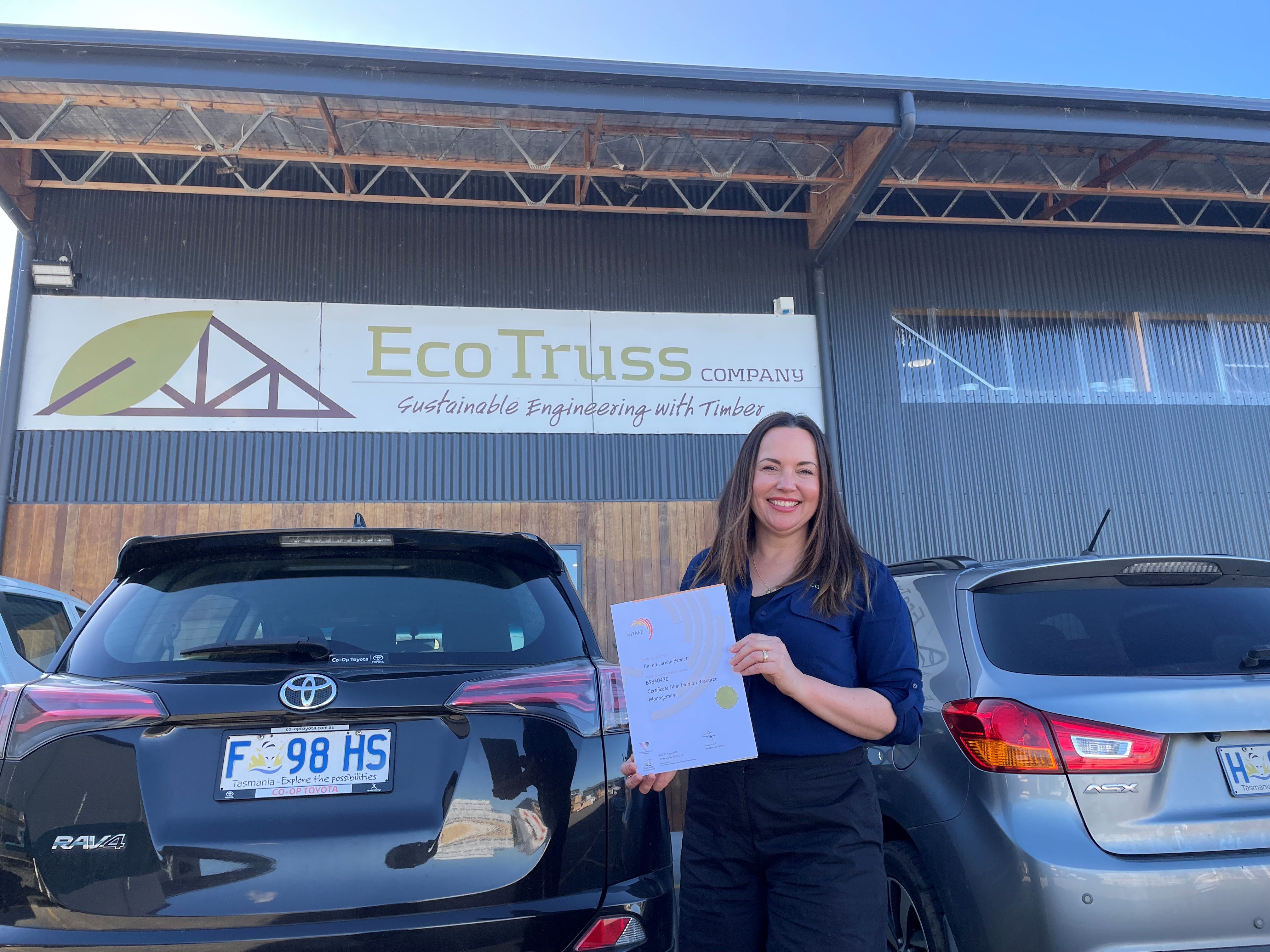 TasTAFE Graduate Holding her certificate in front of her business warehouse