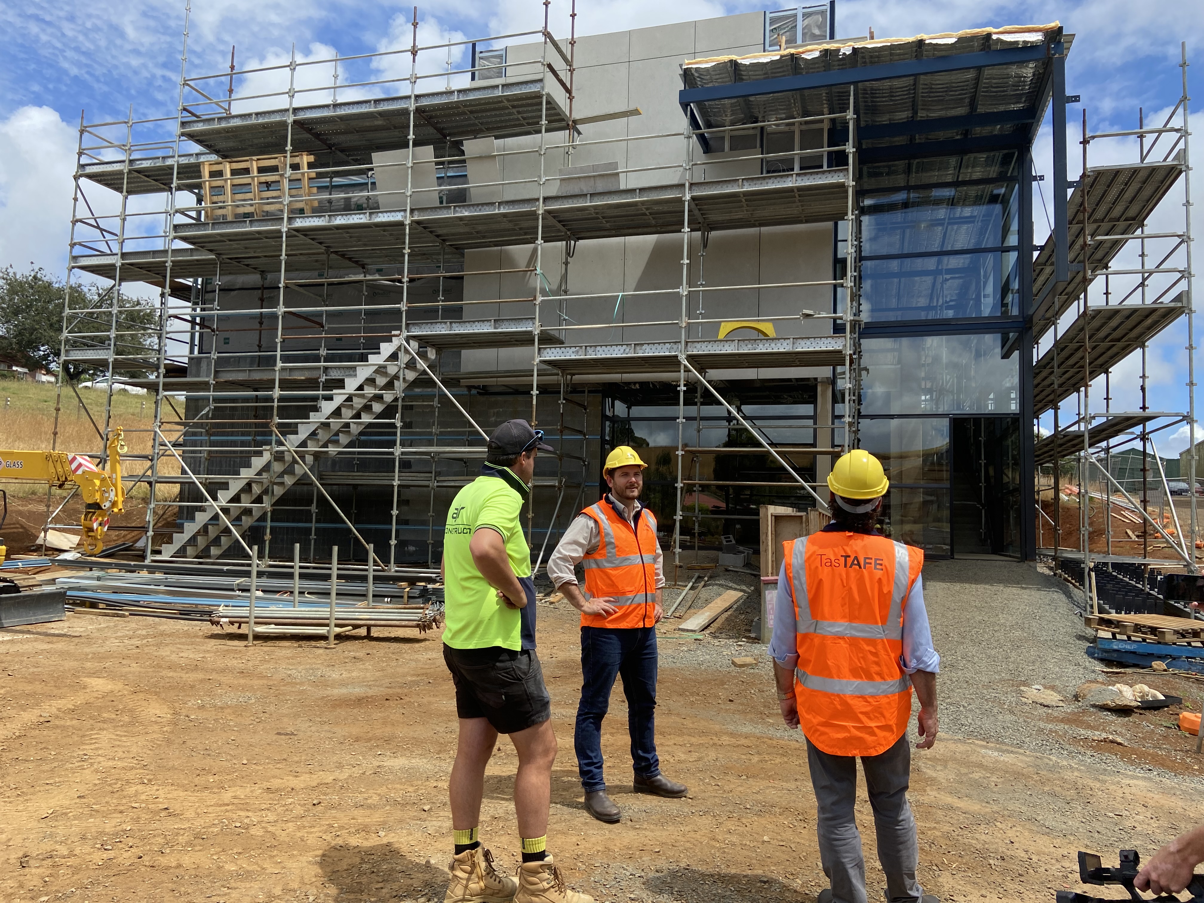 # people standing in front of building construction with scaffolding around the outsides in Hi visibility clothing 