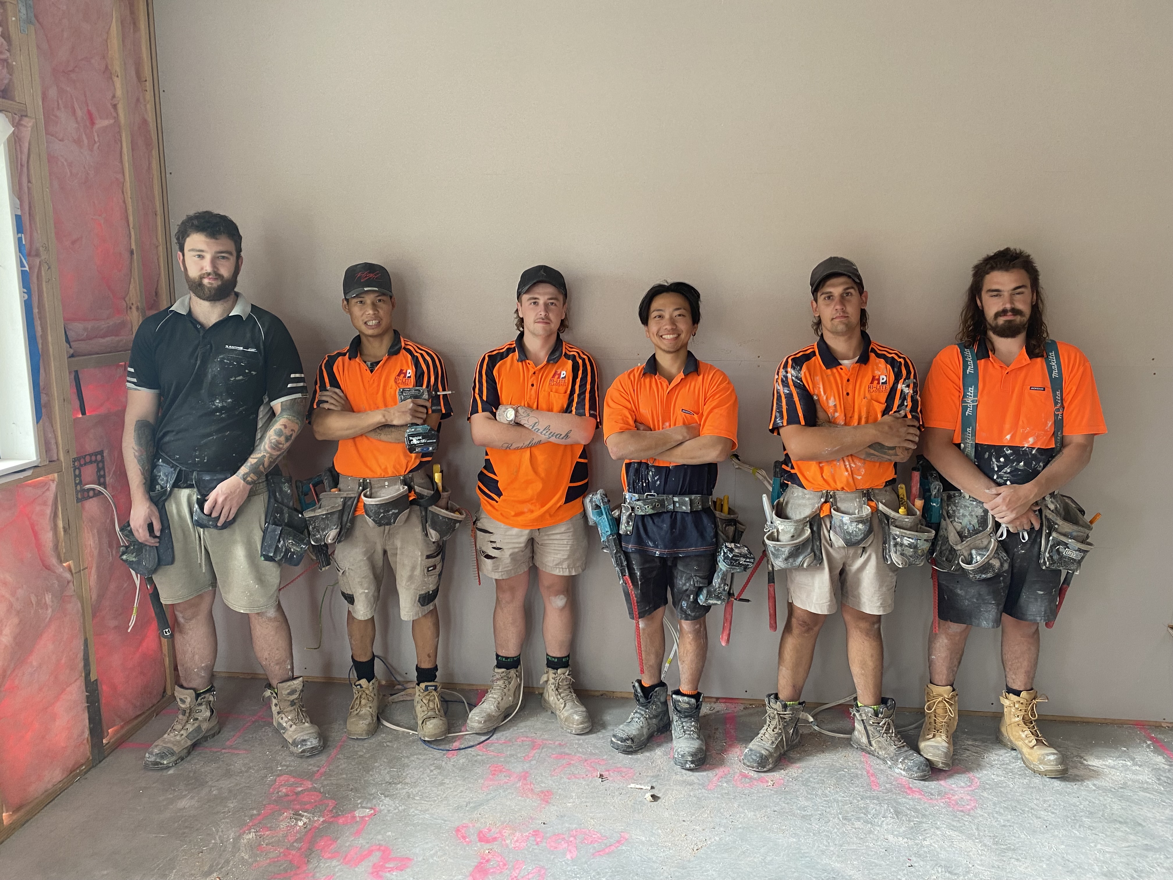 6 people ona building site in their work clothes with hi-vis tops and tool belts on