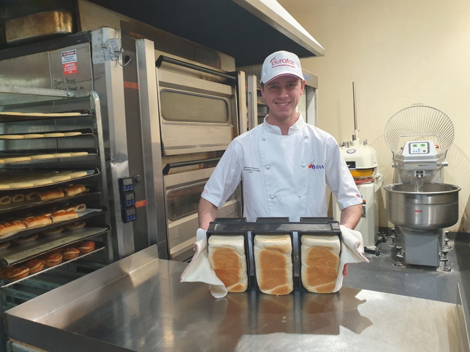 TasTAFE Bakery Apprentice Bjarke Svendsgaard poses in the baking kitchen holding 3 loaves of bread
