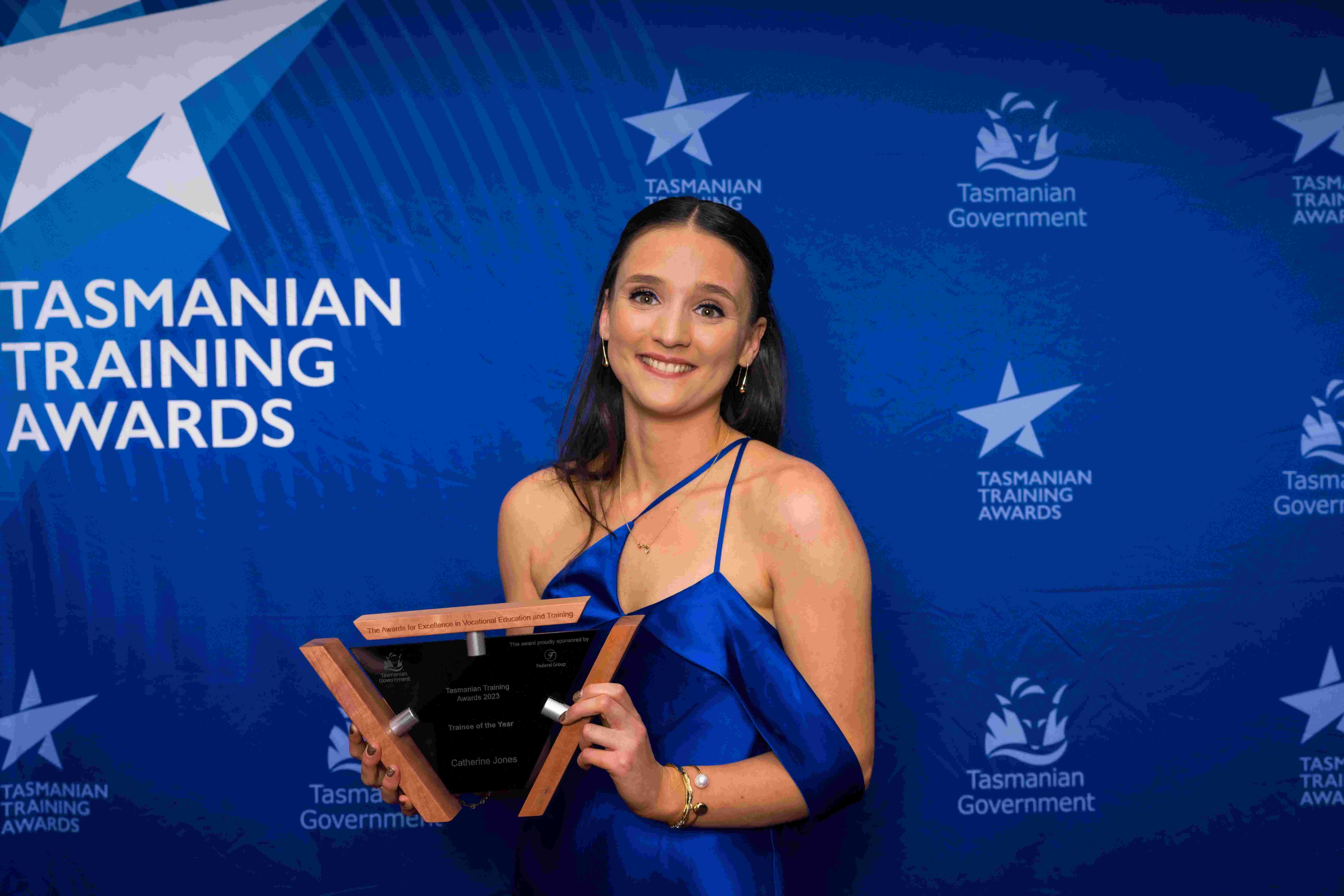 Woman holding a trophy in front of a blue Tasmania Training awards background
