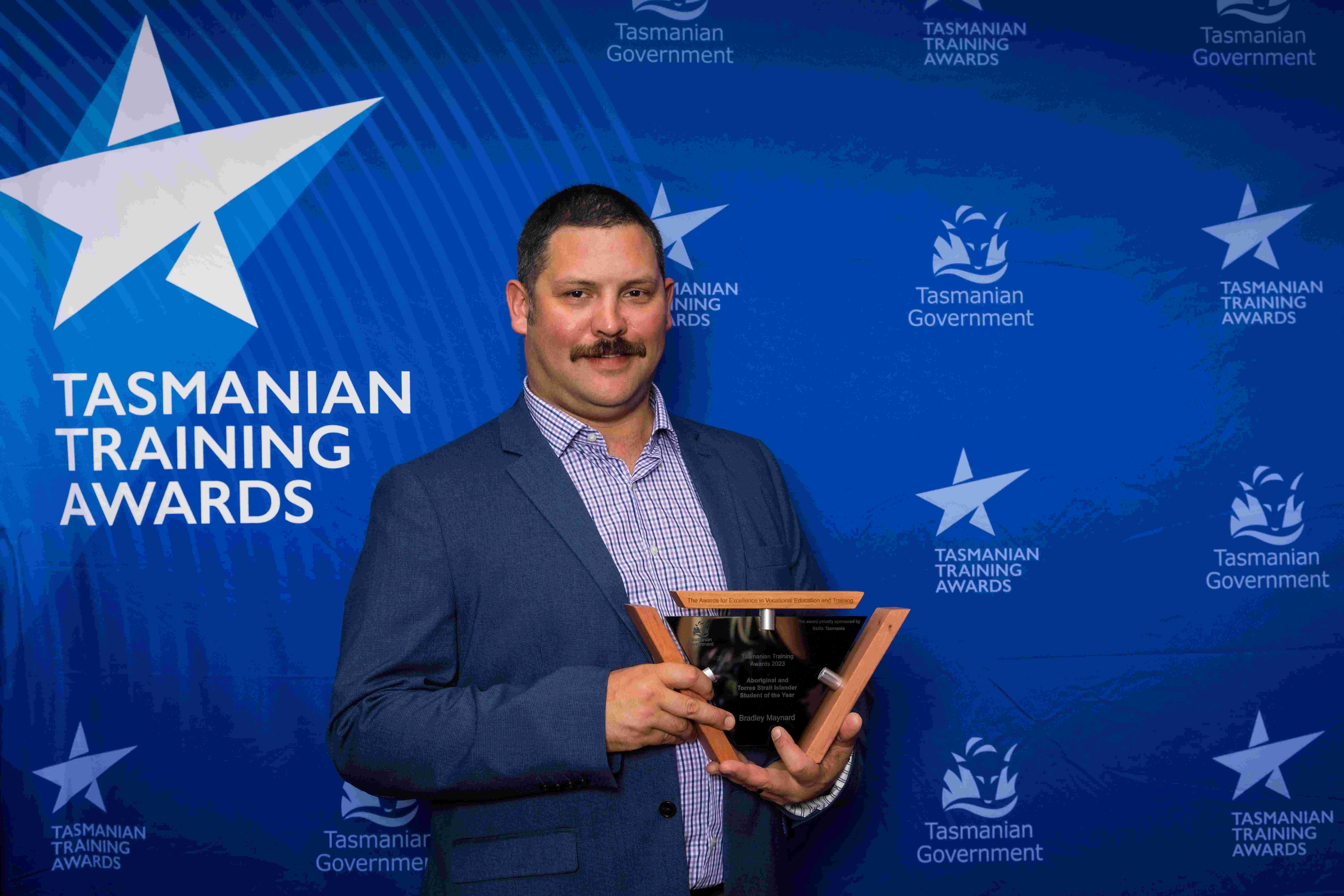 Man holding trophy wit Blue Tasmanian Training awards background