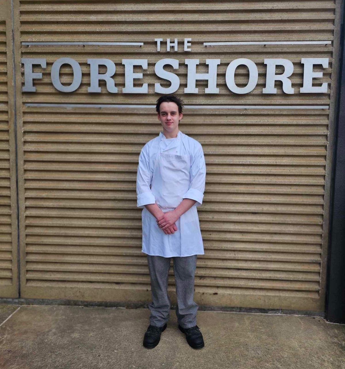 Cookery student in chef clothing standing in front of the Foreshore Hotel building