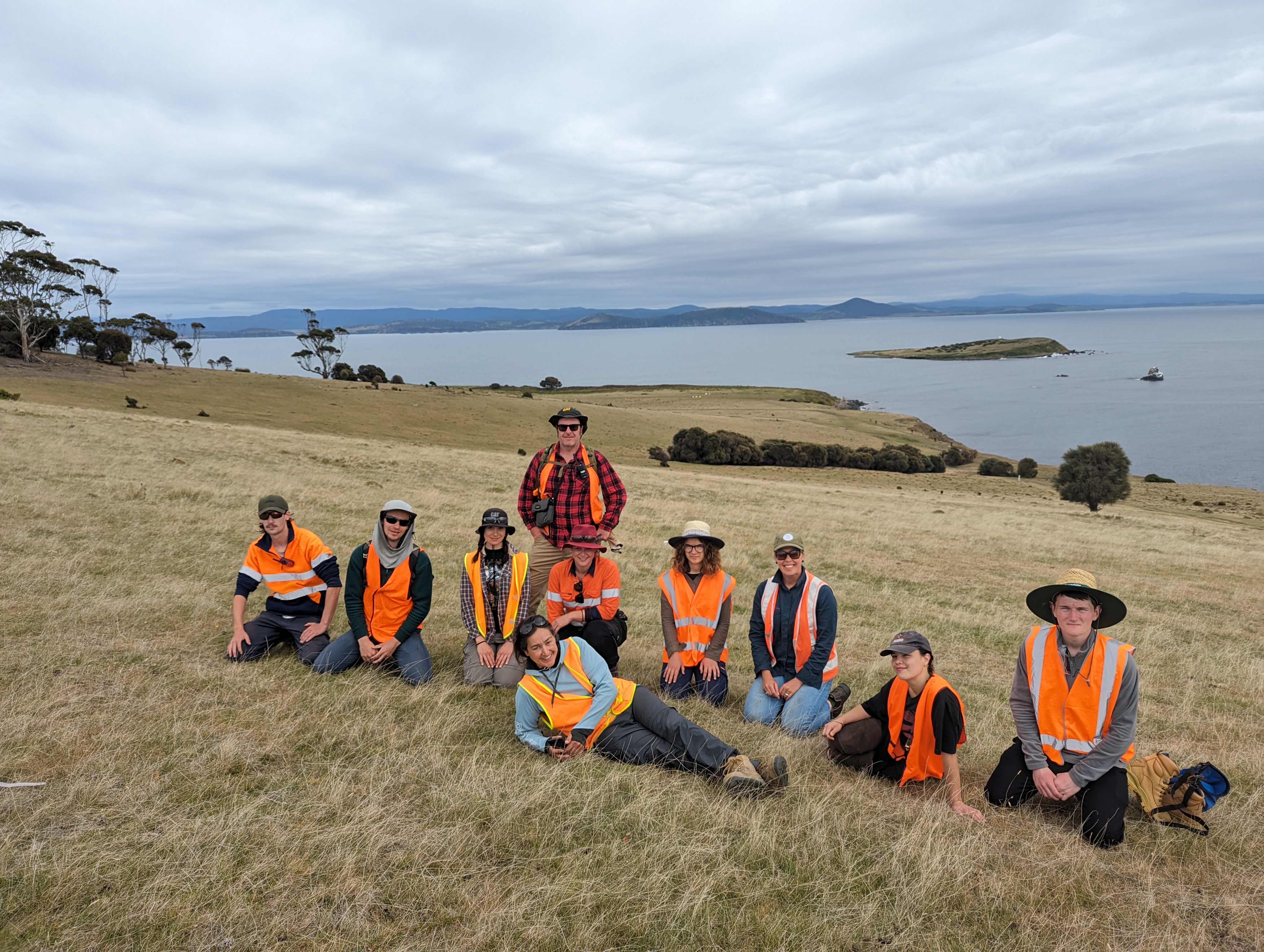 Group of students wearing Hi-vis clothing on the grass and water in the background. 