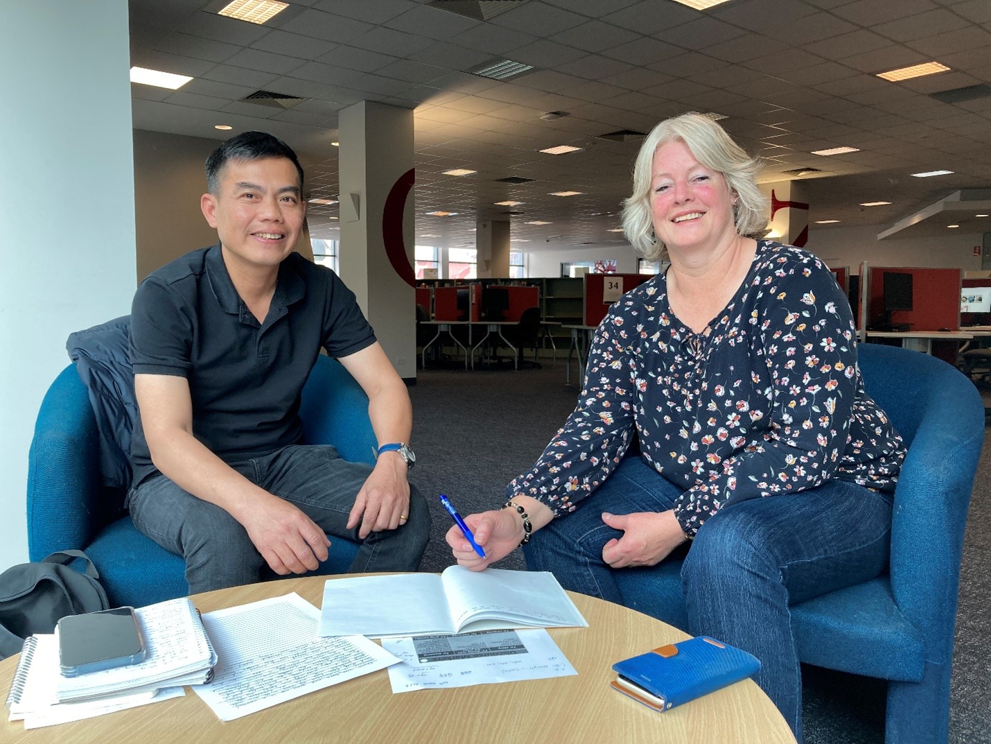 Luu and Michelle pictured in TasTAFE’s Hobart Campus with papers, notebooks and phone on a small round table in front of them. 