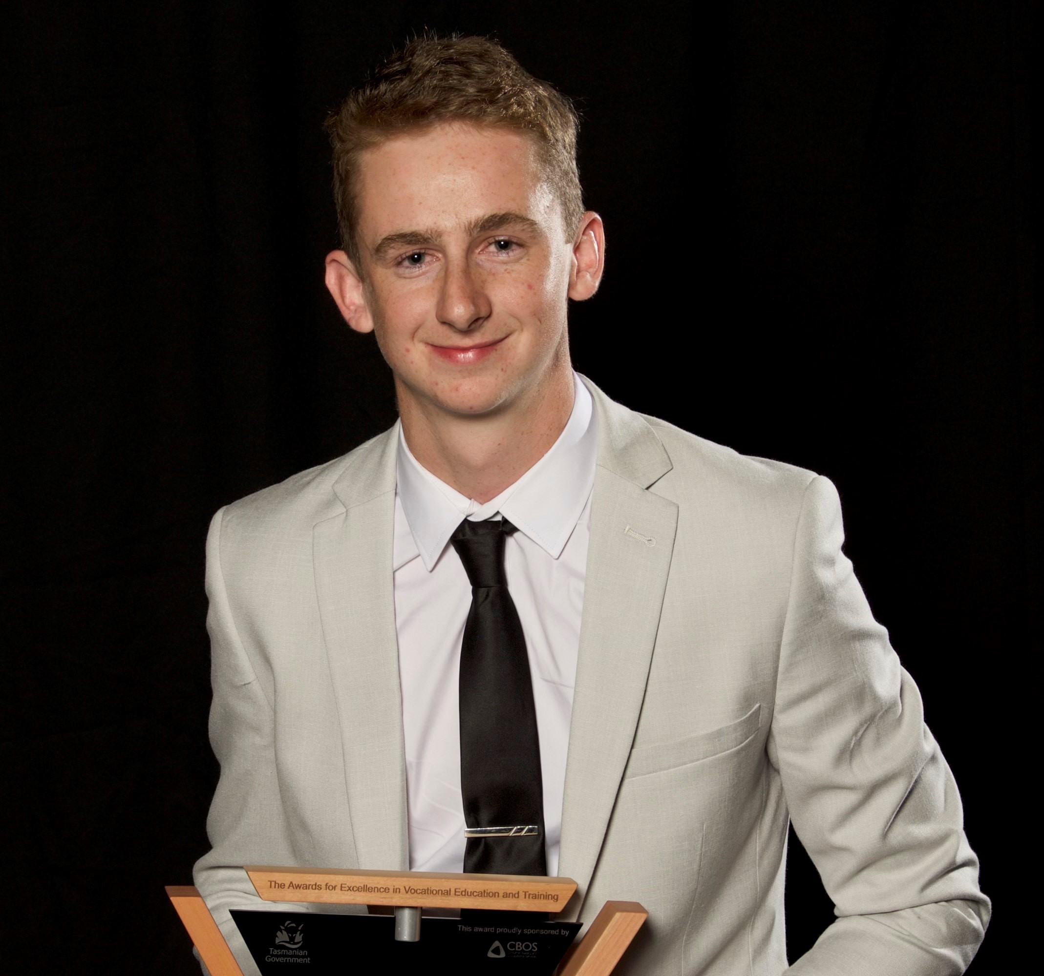 Apprentice of the year posing with his trophy sitting on a stool
