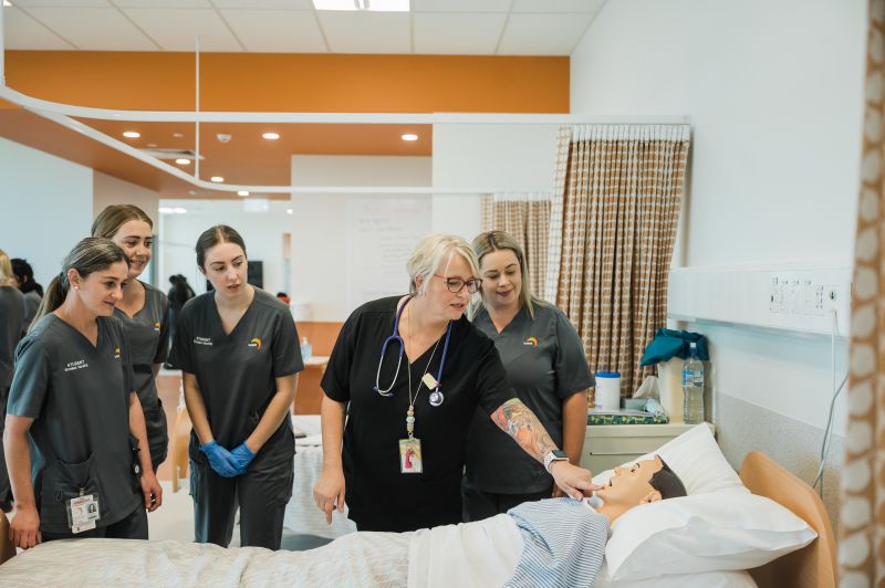 Nursing Teacher checks a dummy's pulse in front of 3 students 