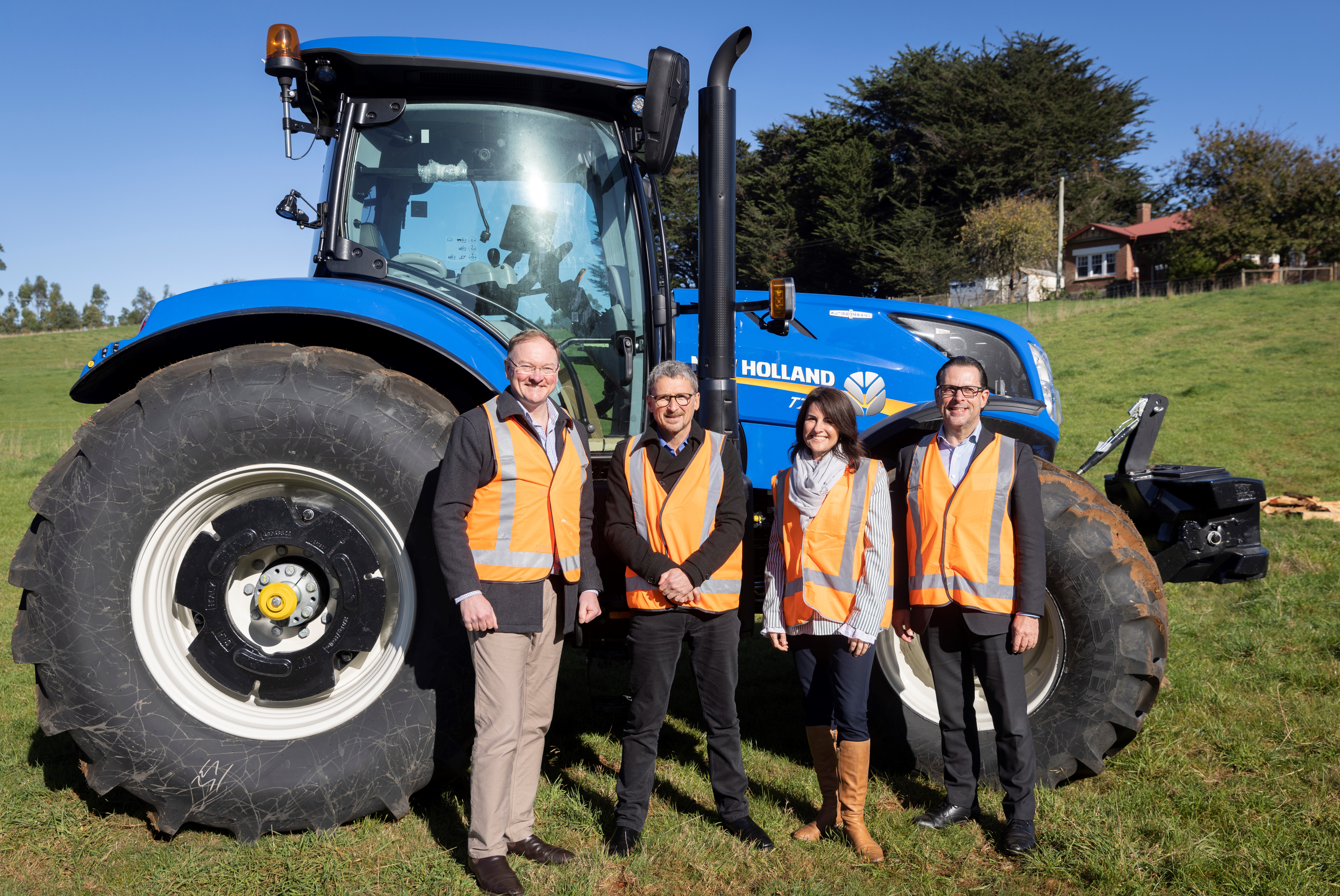 TasTAFE CEO Grant Dreher, minister Jo Palmer, Minister Roger Jaensch and pose for a photo in front of a large blue tractor at TasTAFE's Freer Farm site