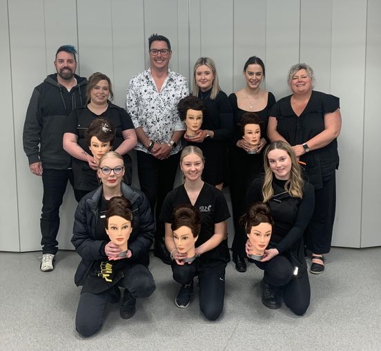 Group photo holding mannequin heads with hair styles created by students