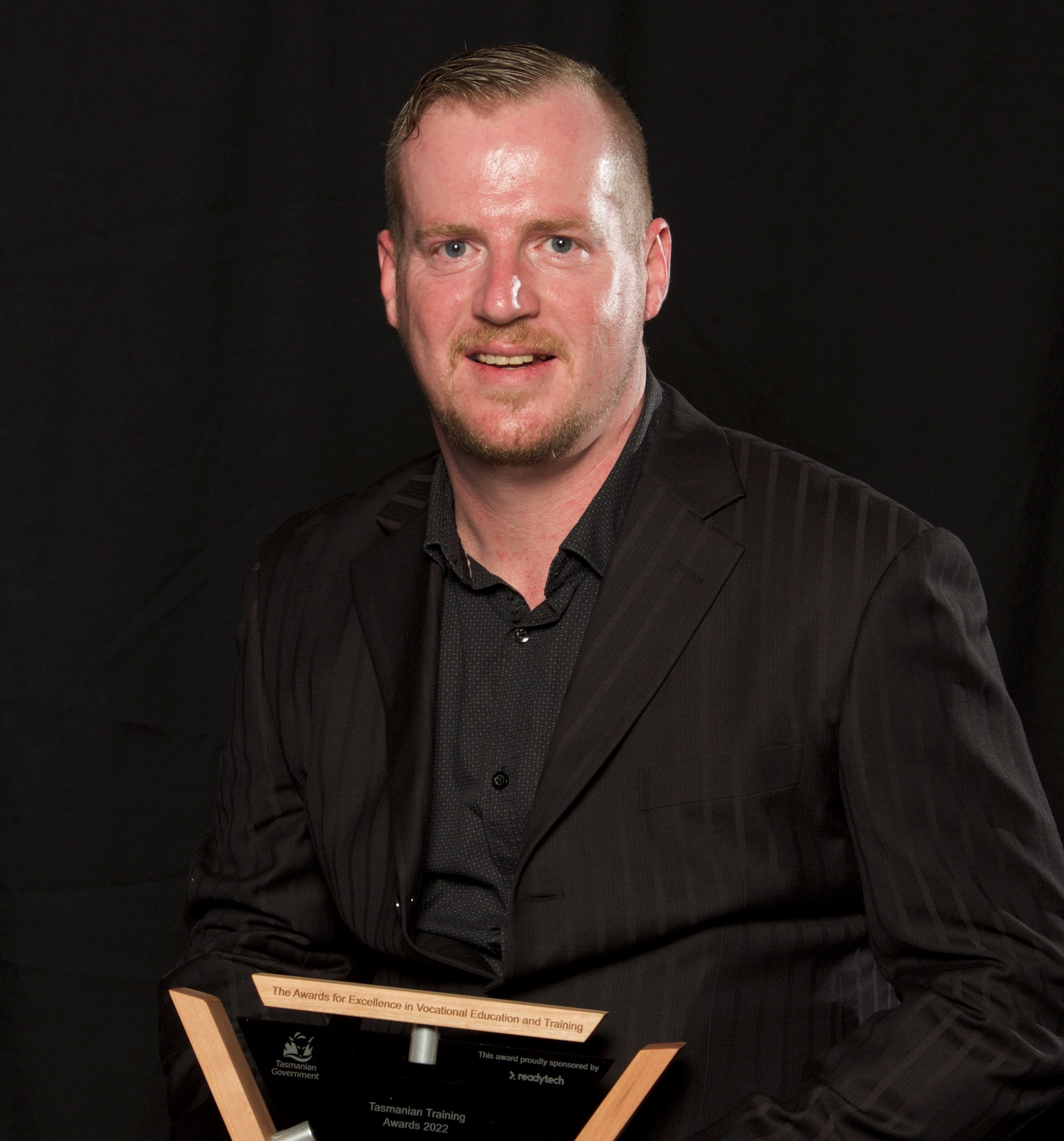 Matthew Fraser – VET Teacher/Trainer of the Year posing with his trophy sitting on a stool