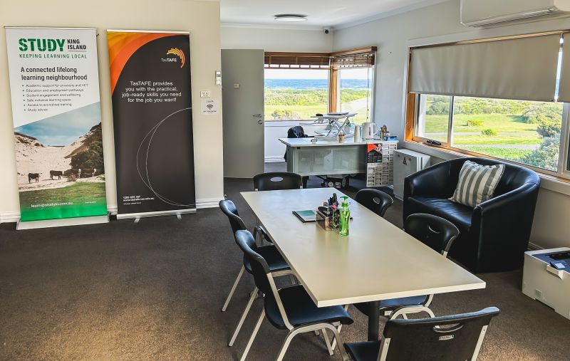 Inside of the King Island Study Hub with a Table, desk and windows with a view of grass and the ocean.