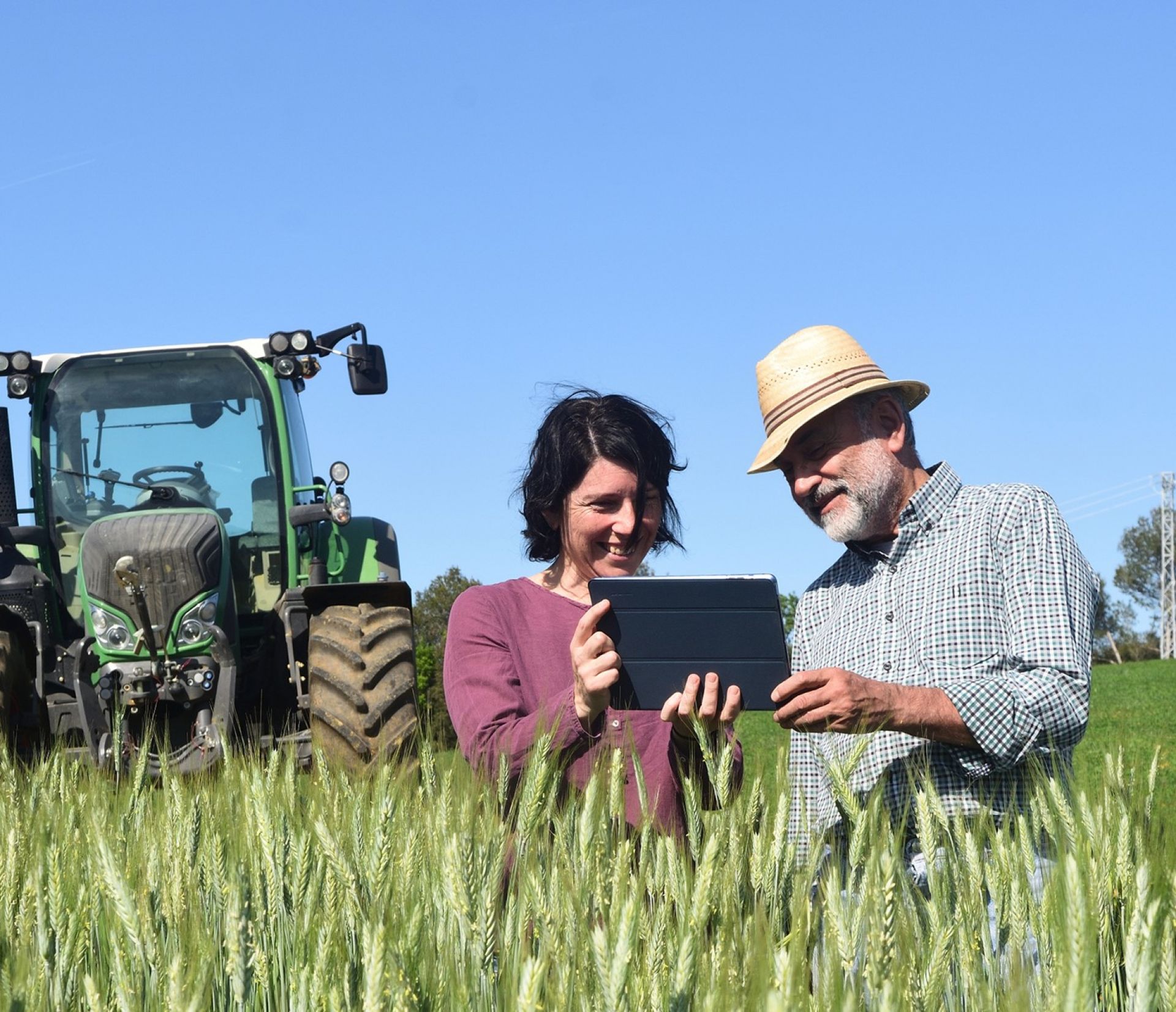 Man and woman with an ipad on the farm with a tractor in the background
