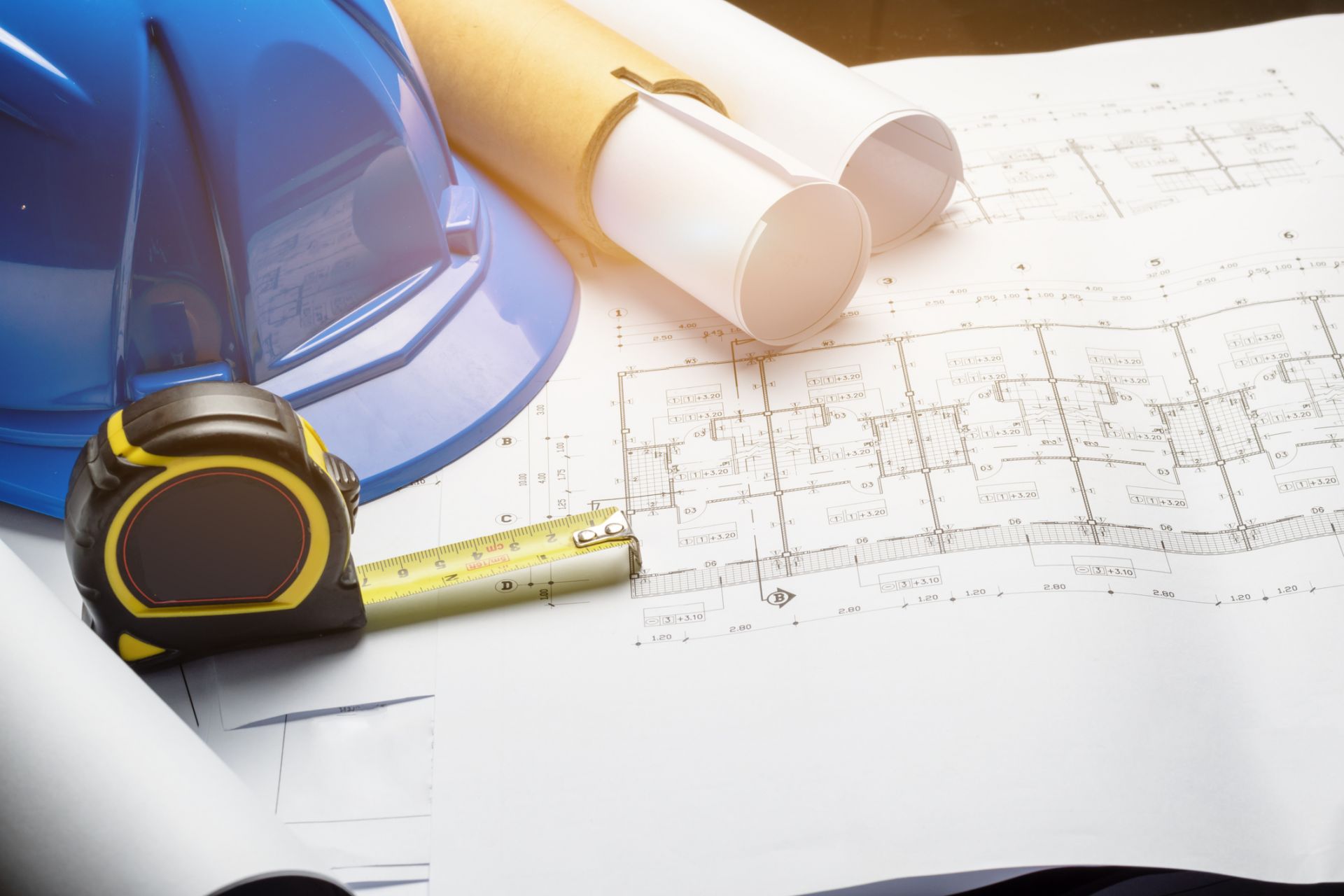 hard hat, measuring tape and engineering plans on a table