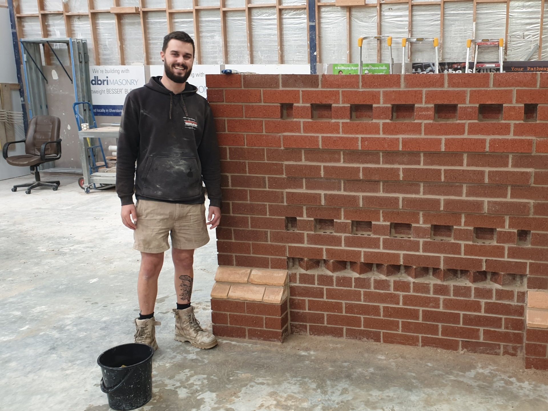 TasTAFE Bricklaying student standing in front of a brick wall he created 