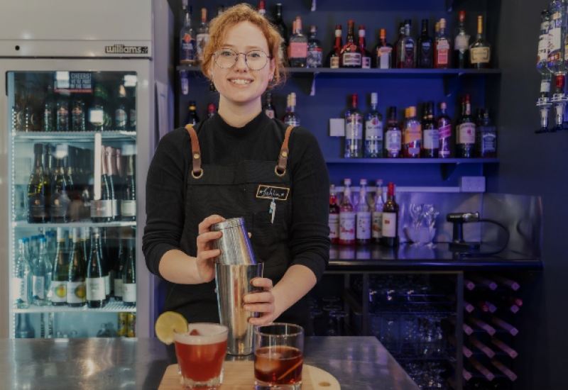Lady making a cocktail holding a cocktail shaker in hospitality clothing