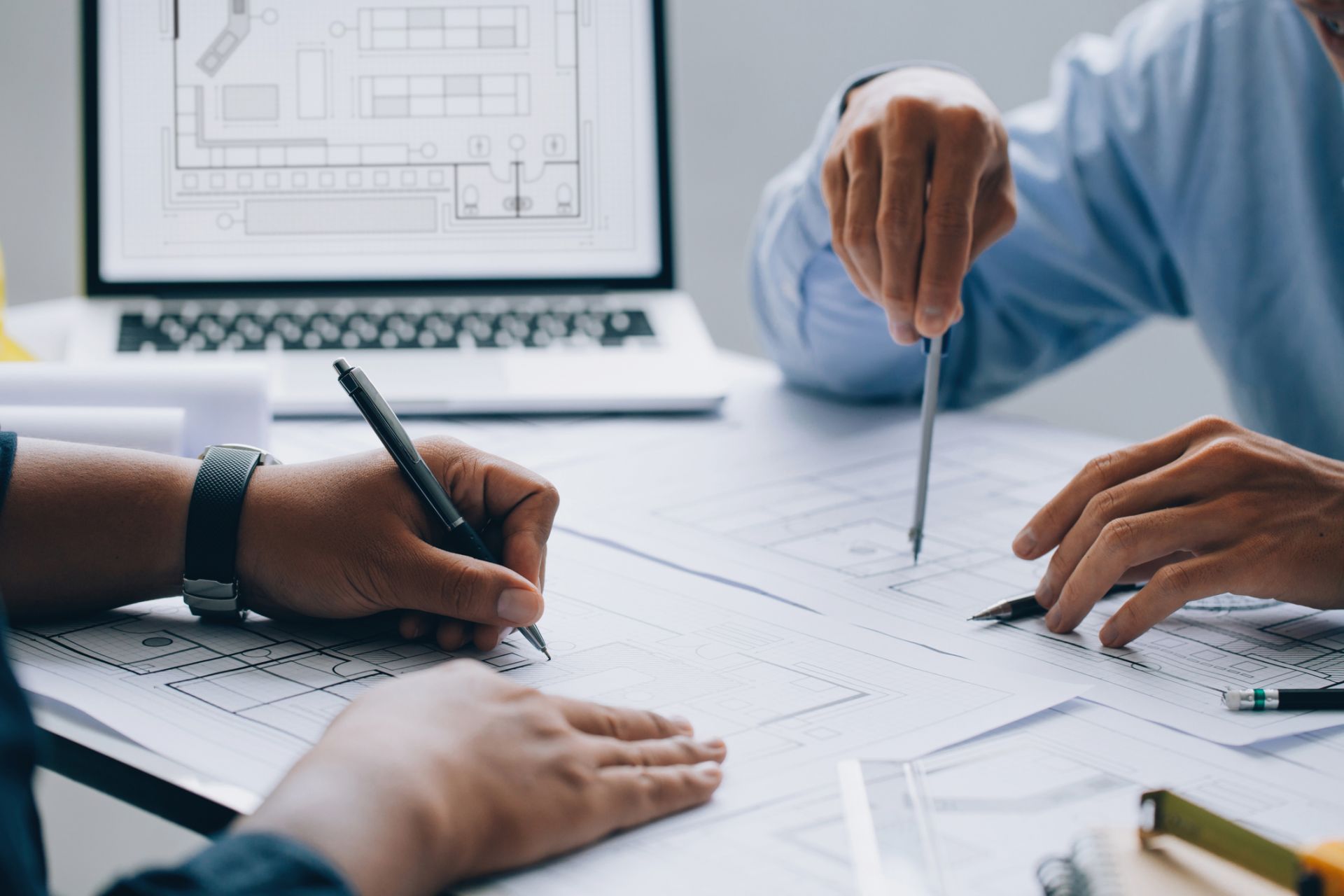 2 people working on building plans in front of a laptop