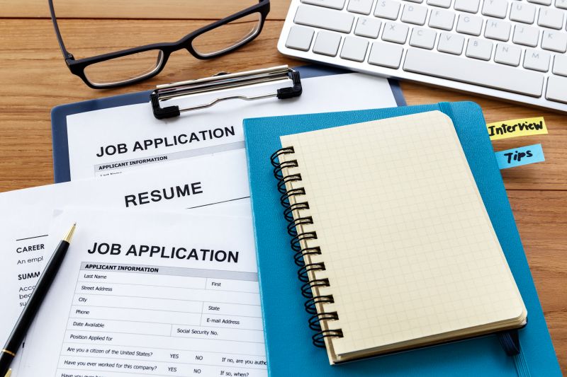 Job application papers with a notebook and laptop messily placed on a desk