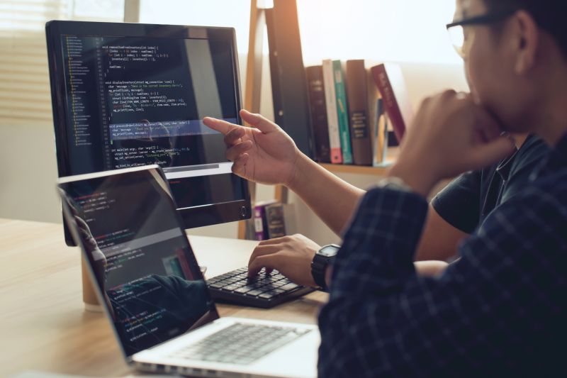 Two people working at a desktop computer with computer code on the screen