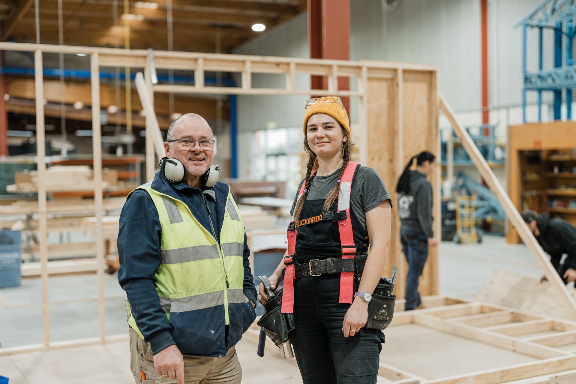Teacher with woman in the construction workshop with house framing in the background 