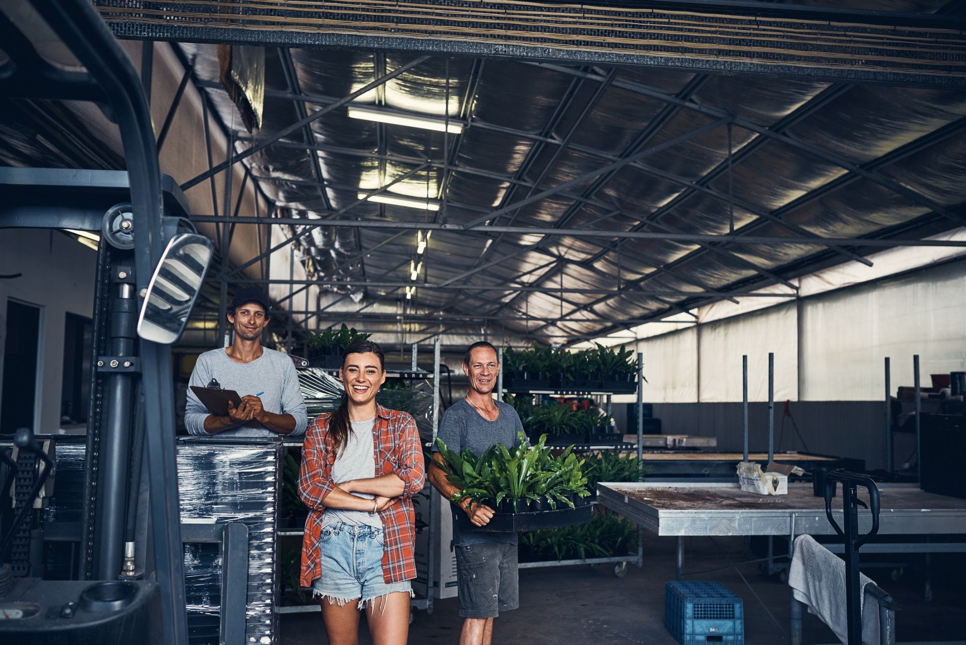 3 people in a plant warehouse in front of a table and forklift