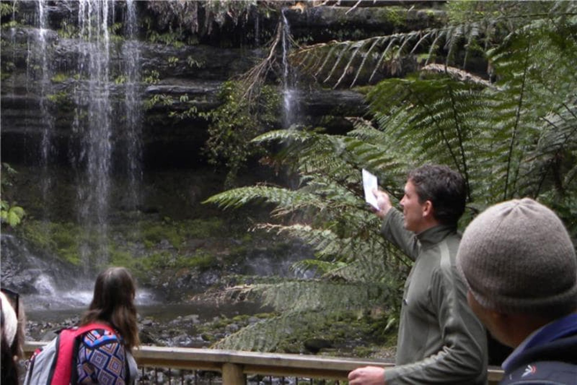 Tour guide with group in front of a waterfall and greenery