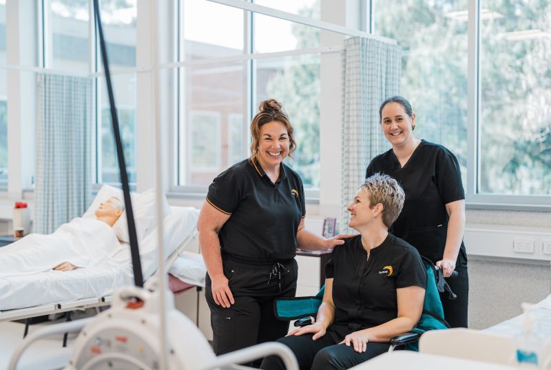 3 Tastafe students, one in a wheelchair with hospital beds in th