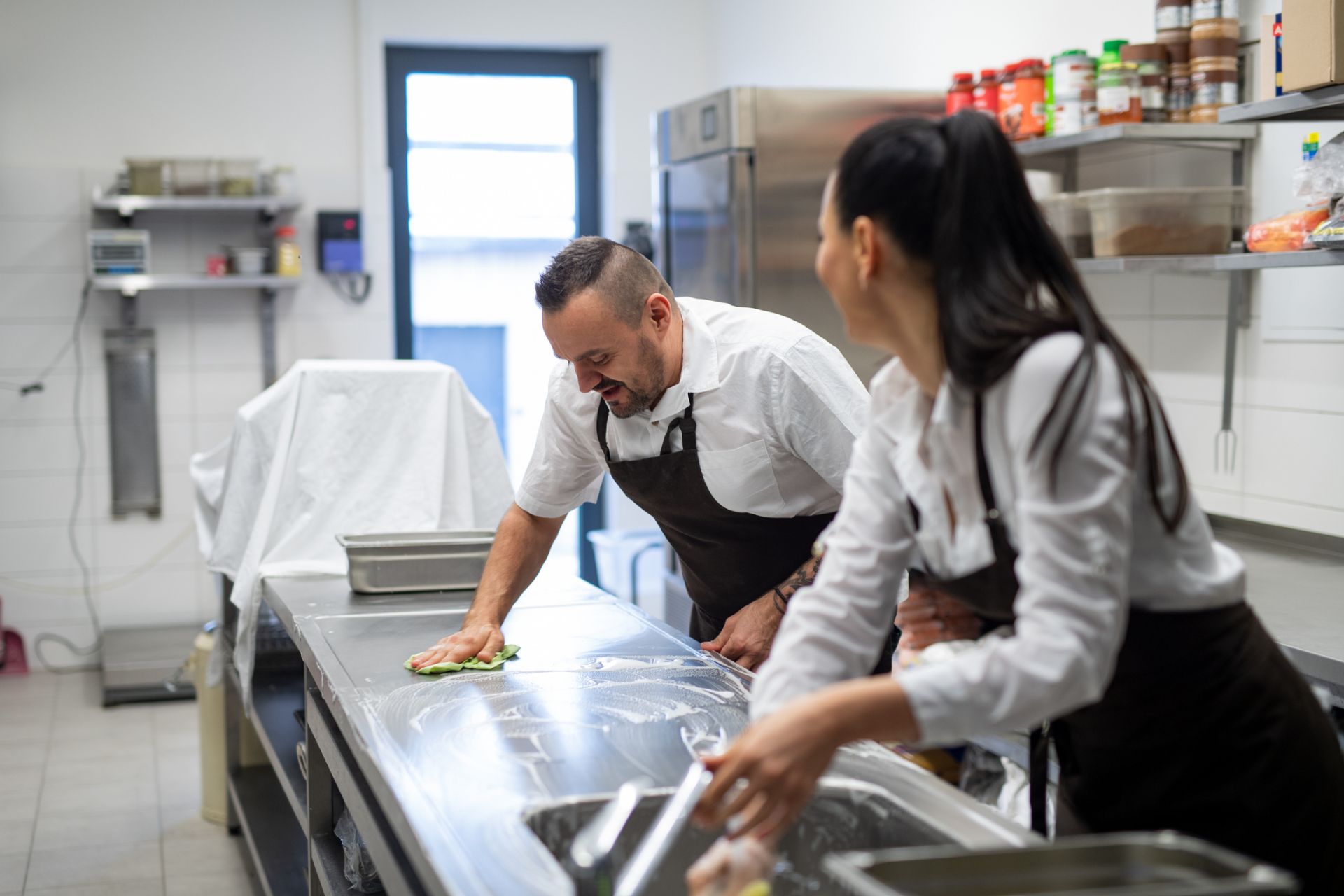 People in chef clothes cleaning a bench in a commercial kitchen