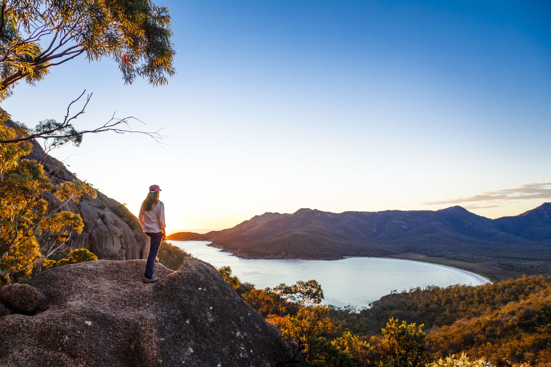 Person standing atop a rock looking over a lake and the wilderness in Tasmania