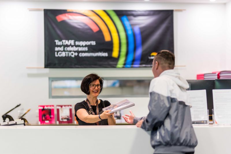 Tastafe staff member at a counter handing a book to a student 