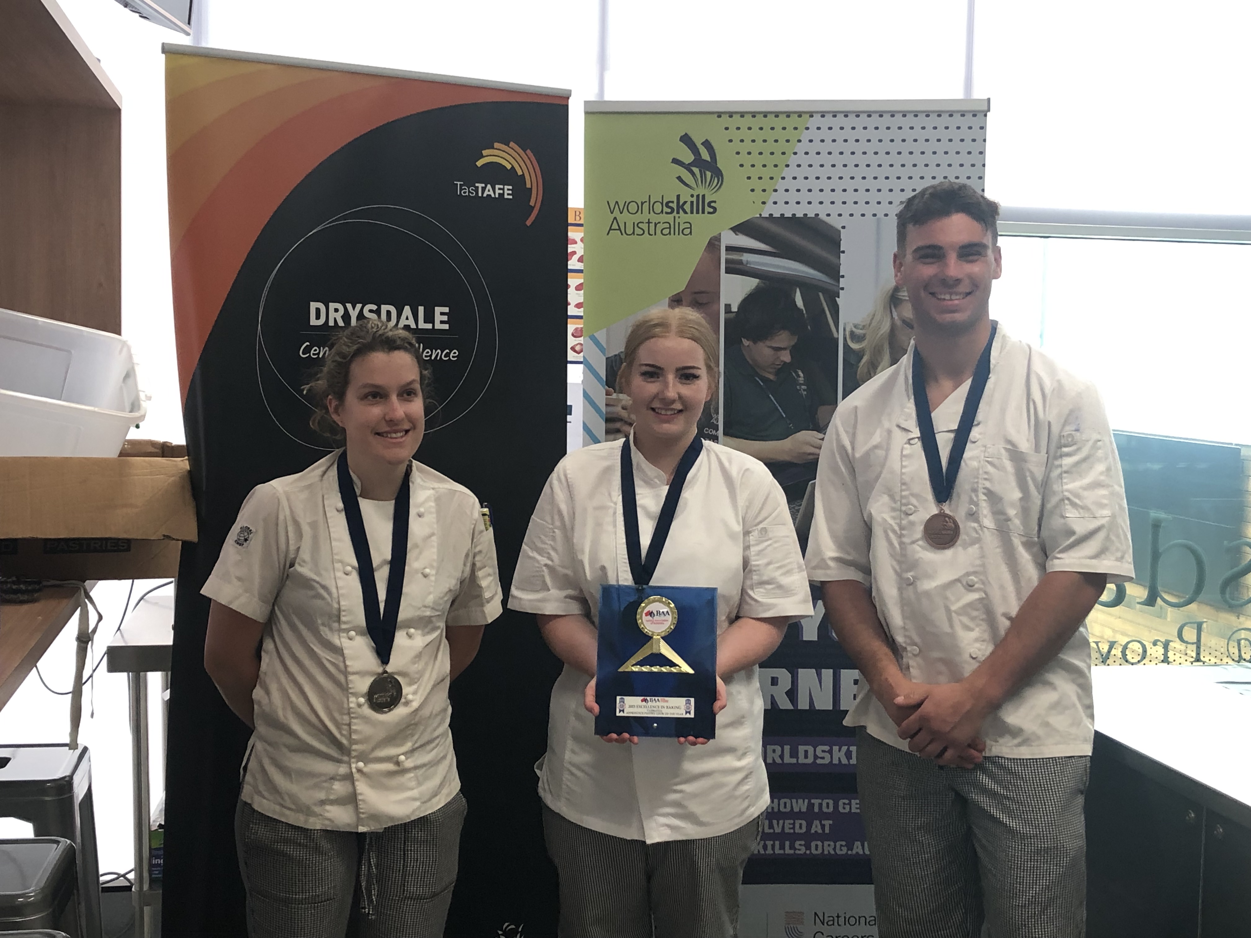 3 people in their chef whites holding a medal