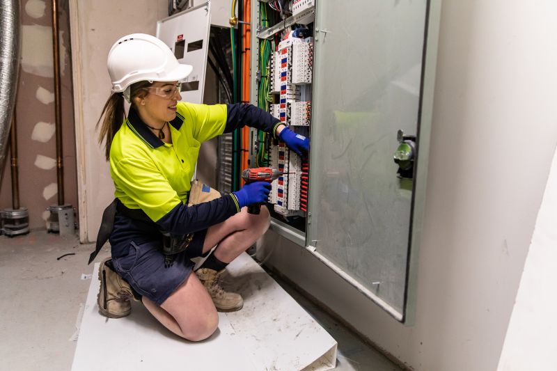 woman working with a drill on an electrical box in hi vis clothing