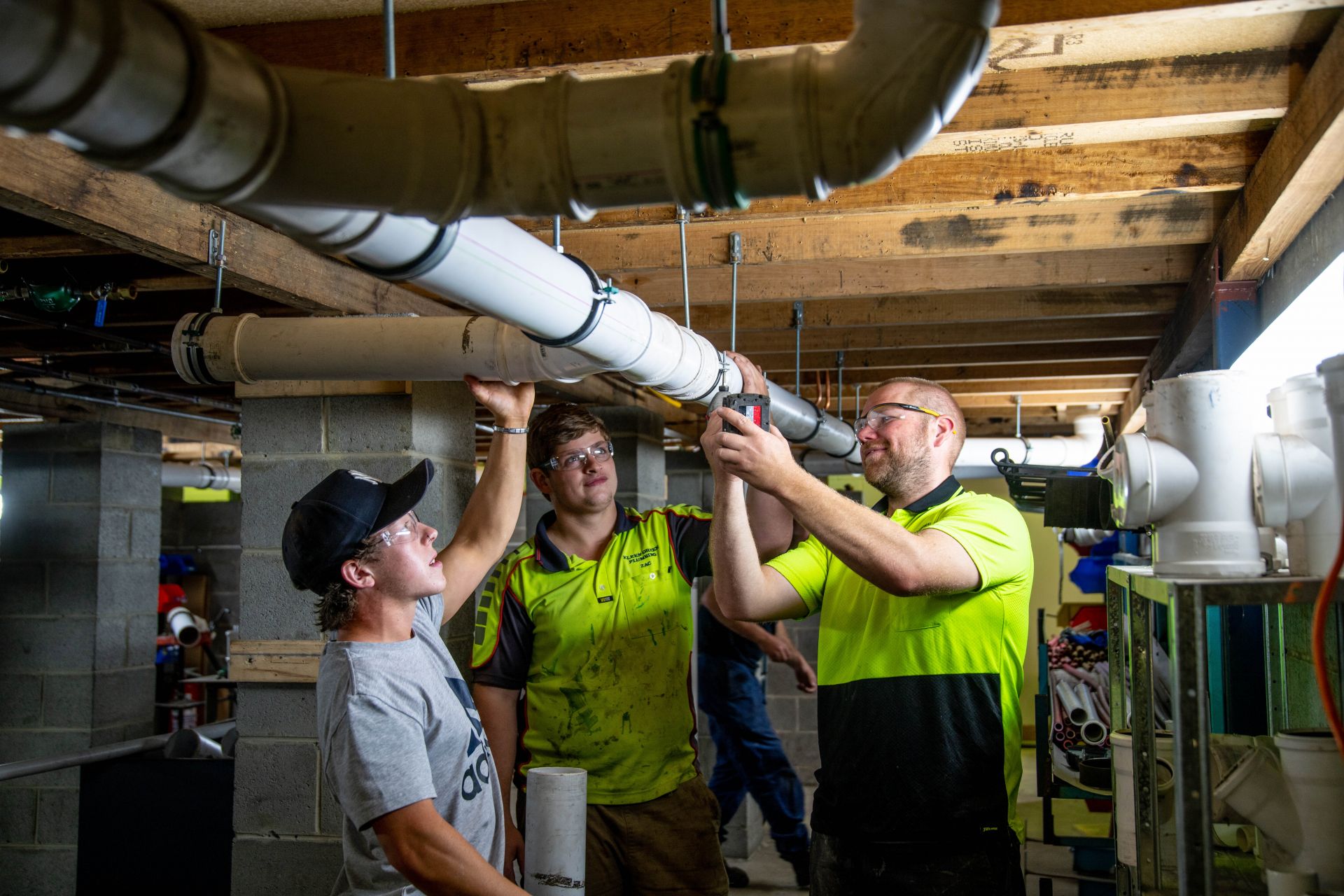 Plumbing students fixing an overhead pipe