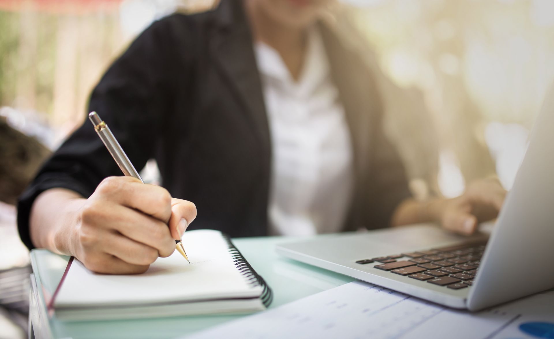 Person sitting in front of a laptop writing in a notebook