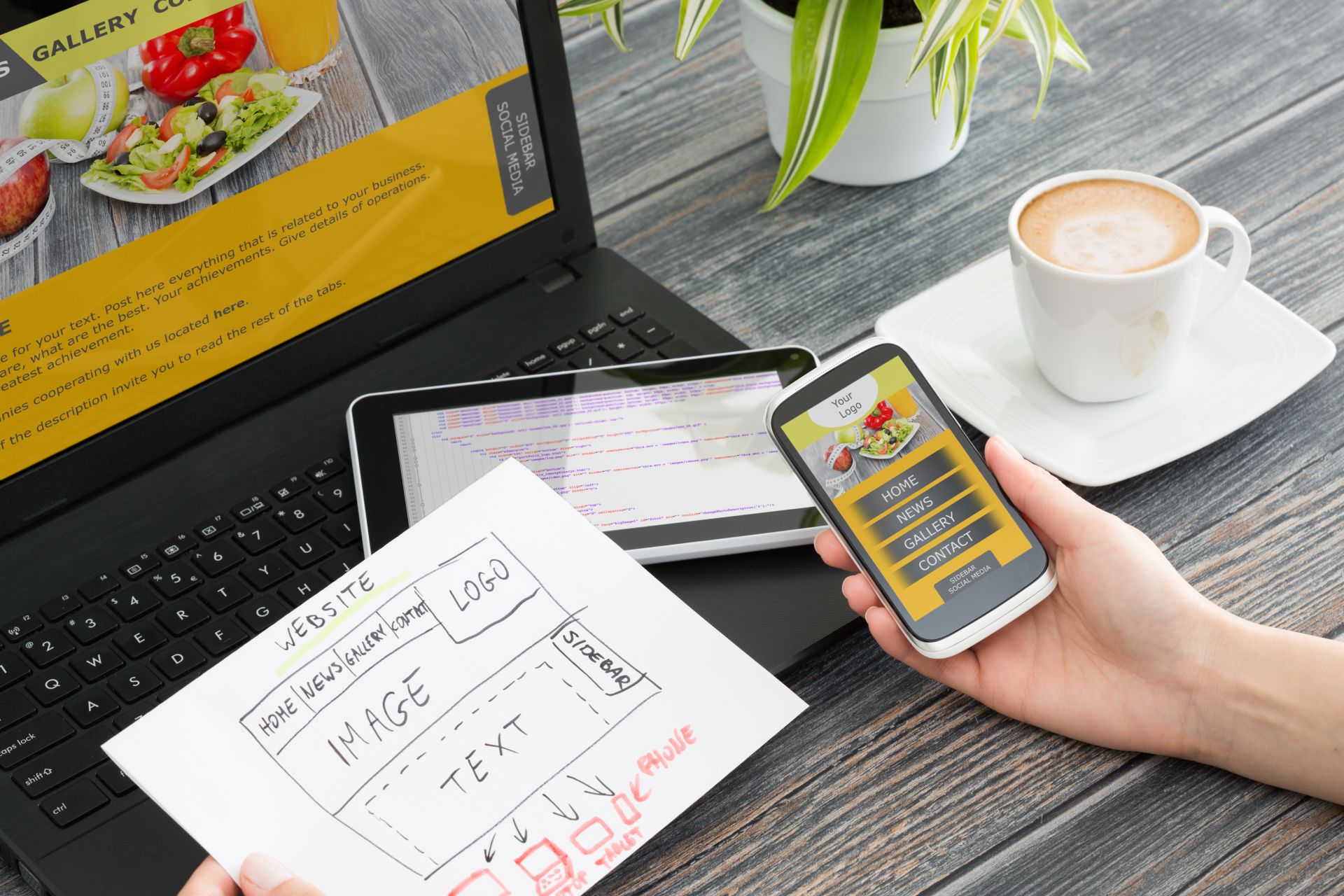 Hands holding a phone and paper in front of a laptop and a tablet on