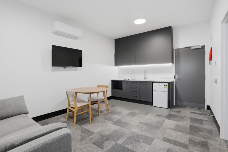 A kitchen with small fridge, dining table and chairs, a couch and a TV