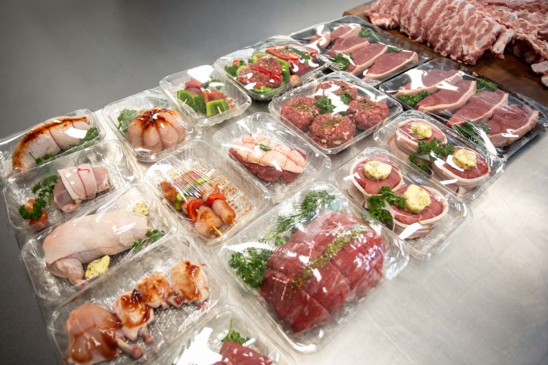 An assortment of value-added meats packaged in plastic trays on a stainless steel counter, ready for retail display.