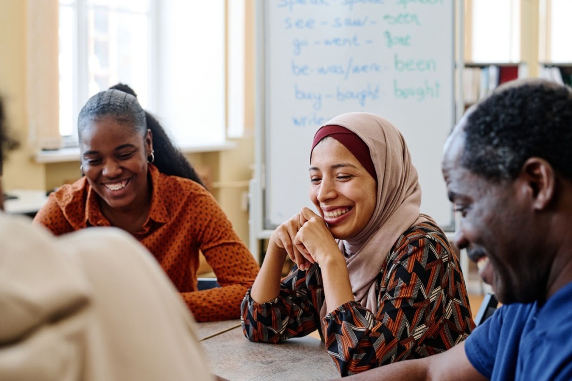 A diverse group of students sitting at a table, laughing together in a classroom